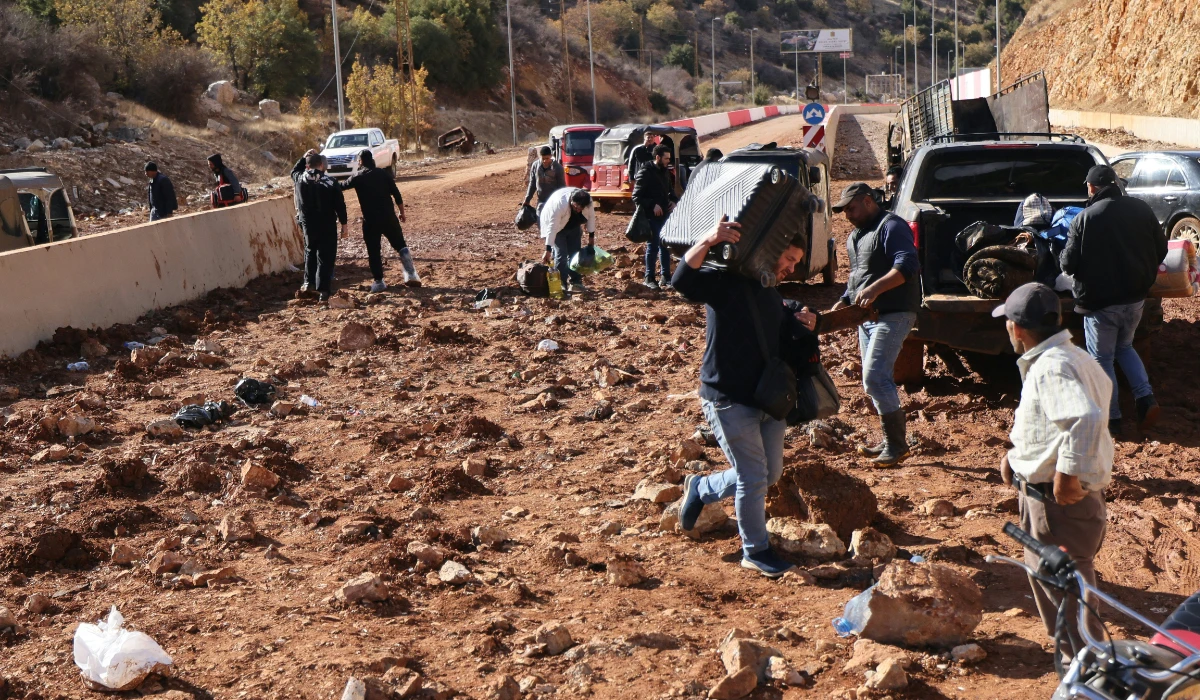People fleeing Israeli bombardment in Lebanon carry their belongings before crossing a crater, caused by an Israeli strike, in the area of Masnaa on the Lebanese side of the border crossing with Syria, on November 20, 2024. (AFP)