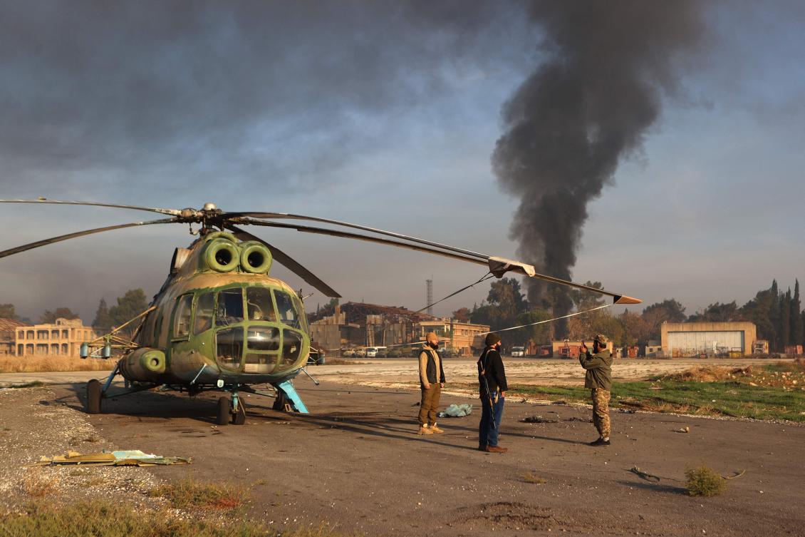 Islamist fighters pose for a picture with an army helicopter on the tarmac at the Nayrab military airport in the northern Syrian city of Aleppo on December 2, 2024. (AFP)