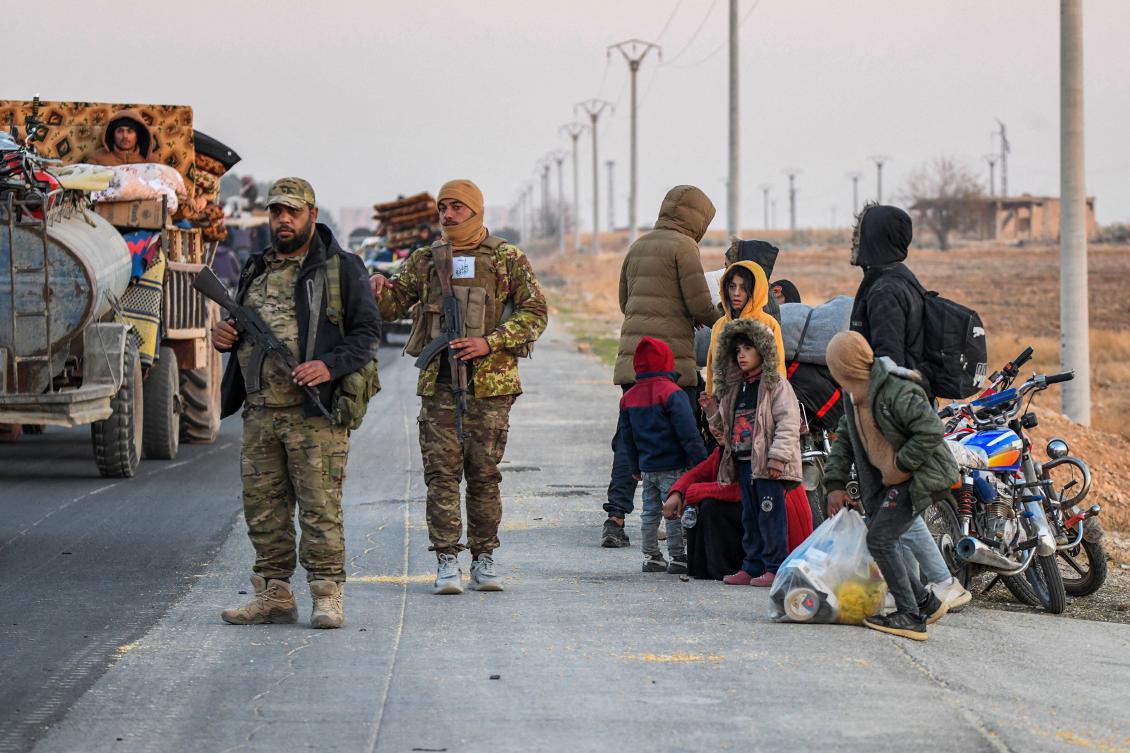 Anti-regime fighters stand on the roadside as displaced Syrian Kurds drive vehicles loaded with belongings on the Aleppo-Raqqa highway to flee areas on the outskirts of the northern city of Aleppo which were formerly controlled by the Kurdish-led Syrian Democratic Forces (SDF), after they were seized by Islamist-led rebels on December 2, 2024. (AFP)