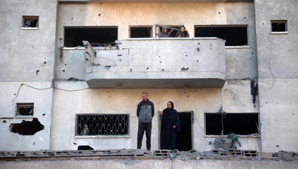 Palestinians stand on the balcony of a damaged flat in front of a building destroyed in an Israeli airstrike in Nuseirat in the central Gaza Stri, Dec. 1 (AFP)