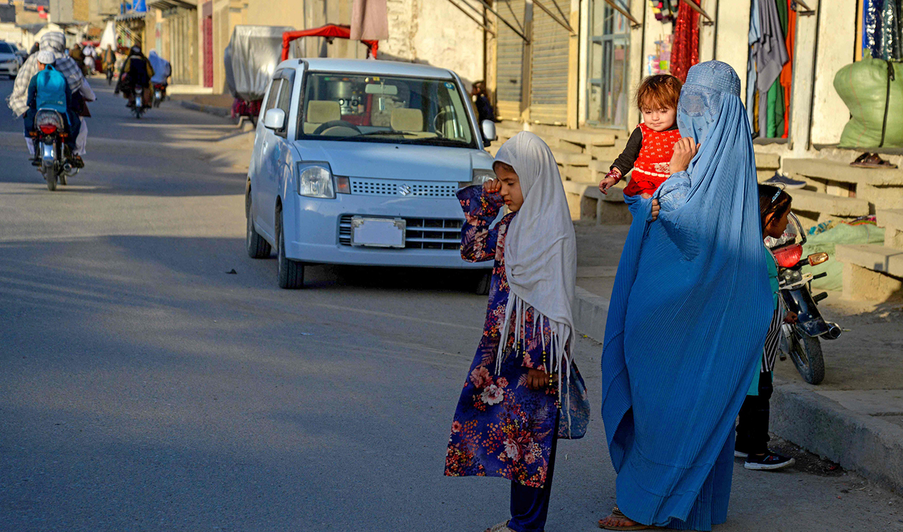 An Afghan burqa-clad woman and children wait along a street in Kandahar on December 3, 2024. (AFP)