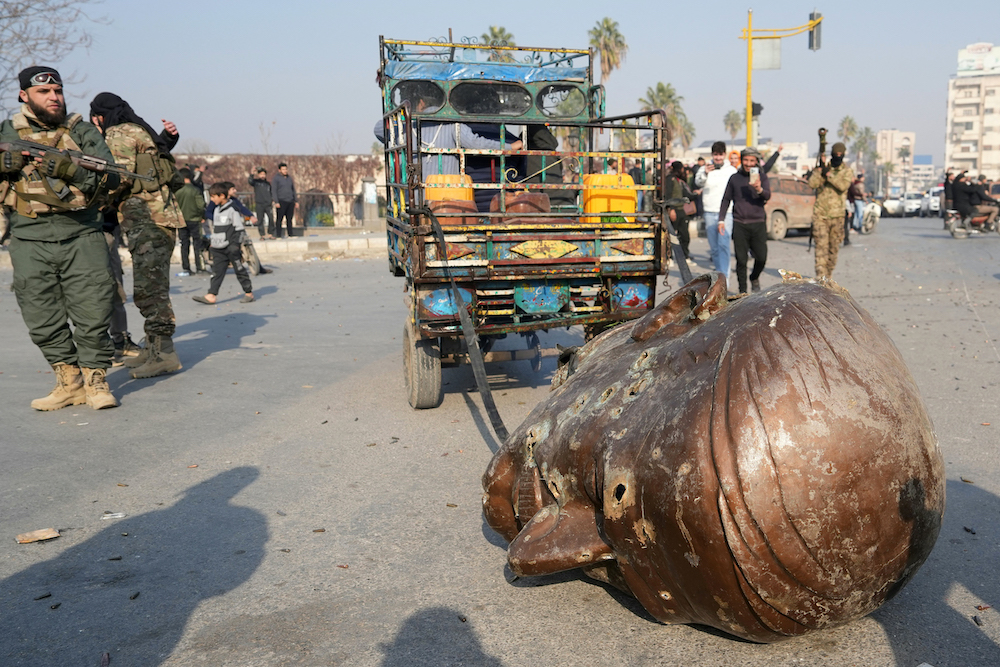 A truck pulls the head from the toppled statue of late Syrian president Hafez Al-Assad through the streets of the captured Syrian city of Hama. (AFP)