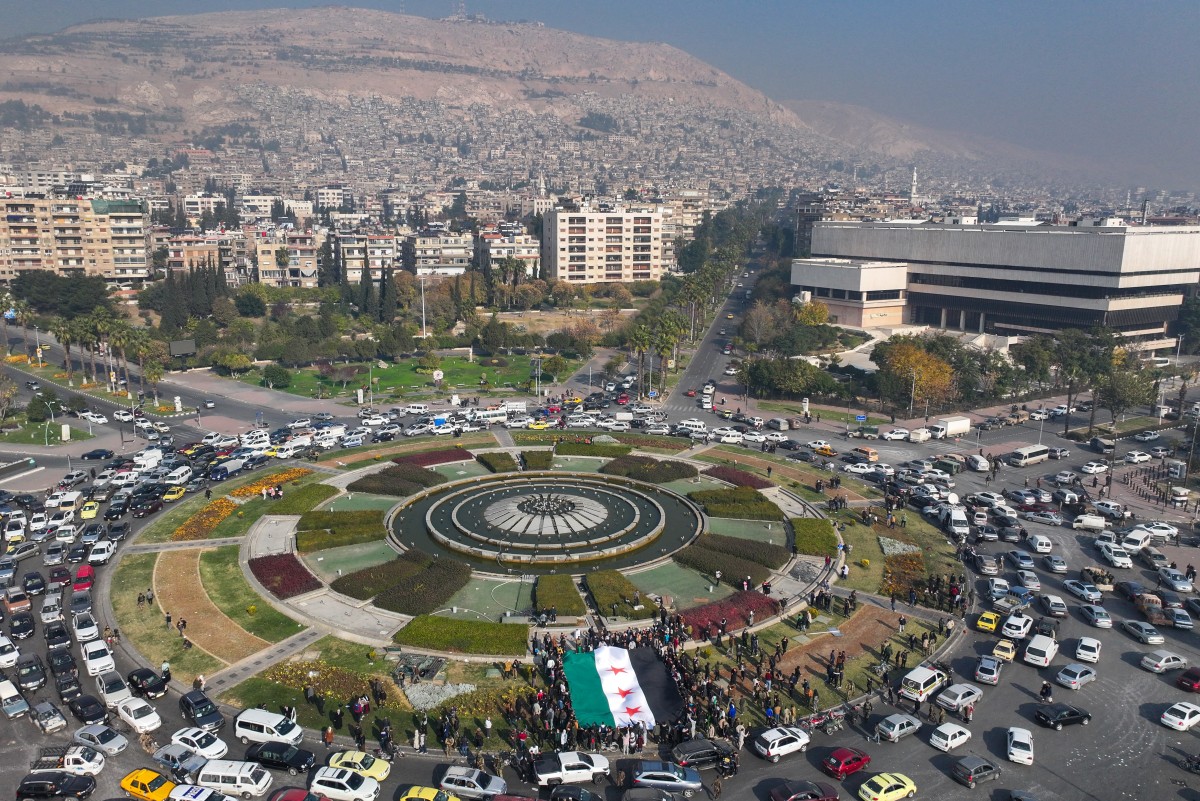 People hold a large Syrian opposition flag at Umayyad Square in Damascus on December 9, 2024. Syrians flocked to the main square of the capital city Damascus on December 9 to mark what many regard as a long-awaited new dawn after the fall of president Bashar al-Assad. (AFP)