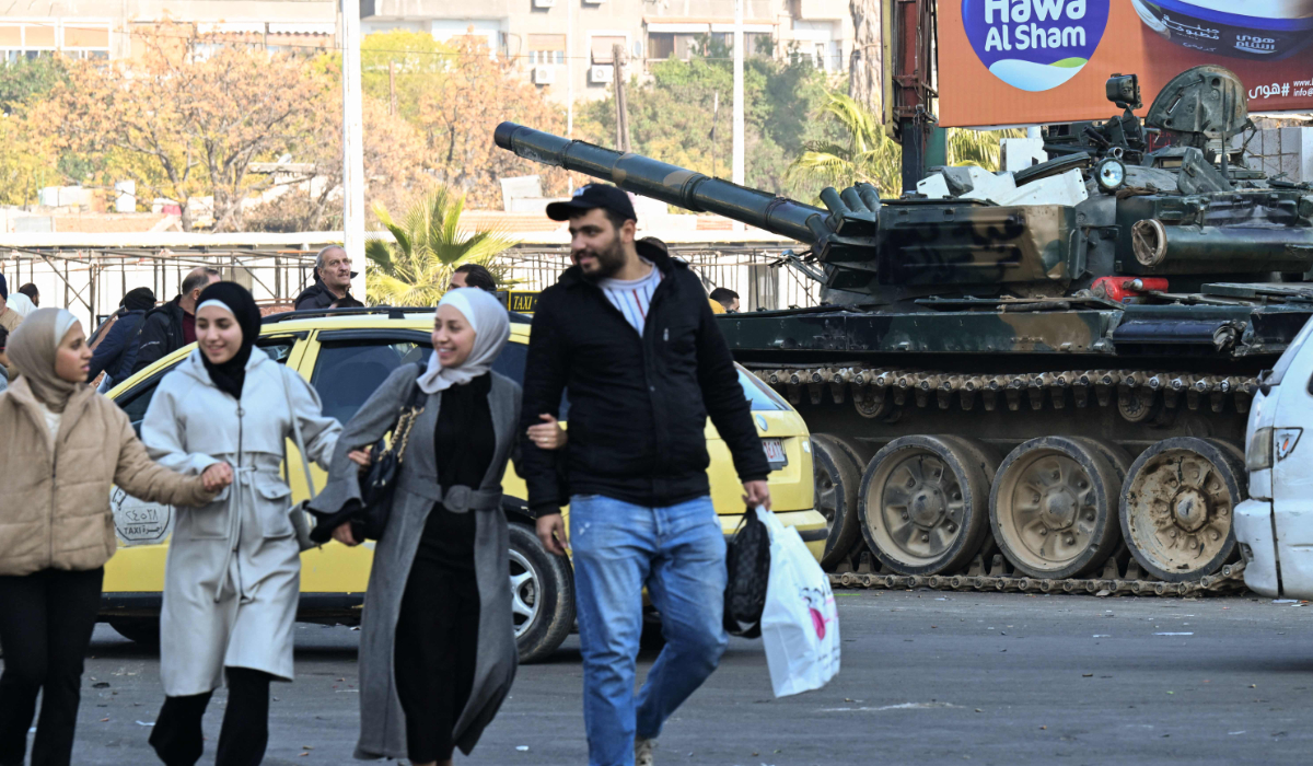People walk past anti government forces securing the Syrian capital in Damascus, on December 9, 2024. (AFP)