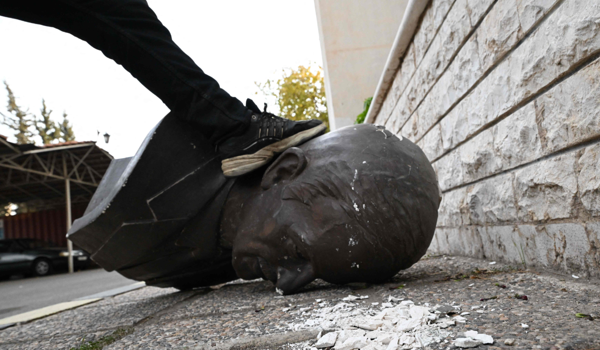 An anti-government fighter steps on the head of a statue of late Syrian president Hafez al-Assad that was brought down outside the Defence Ministry's military security headquarters in the Damascus district of Kafr Sousa on December 9, 2024. (AFP)