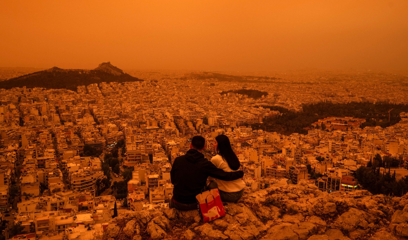 A couple sits on Tourkovounia hill, as southerly winds carry waves of Saharan dust, in Athens, on April 23, 2024. (AFP)