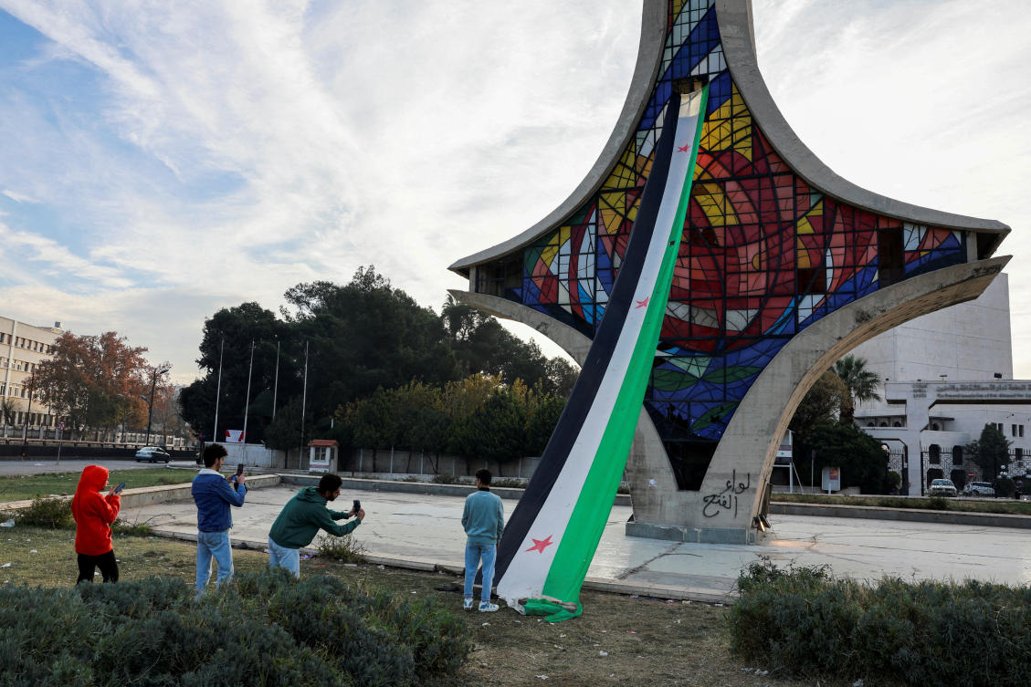 People take pictures next to a Syrian opposition flag in Damascus on Dec. 12, 2024, days after the ouster of President Bashar Assad. (Reuters)