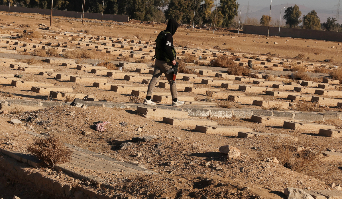 A fighter of the ruling Syrian body walks, as people inspect the site of a mass grave from the rule of Syria's Bashar al-Assad, according to residents, after the ousting of al-Assad, in Najha, Syria, December 15, 2024. (REUTERS)