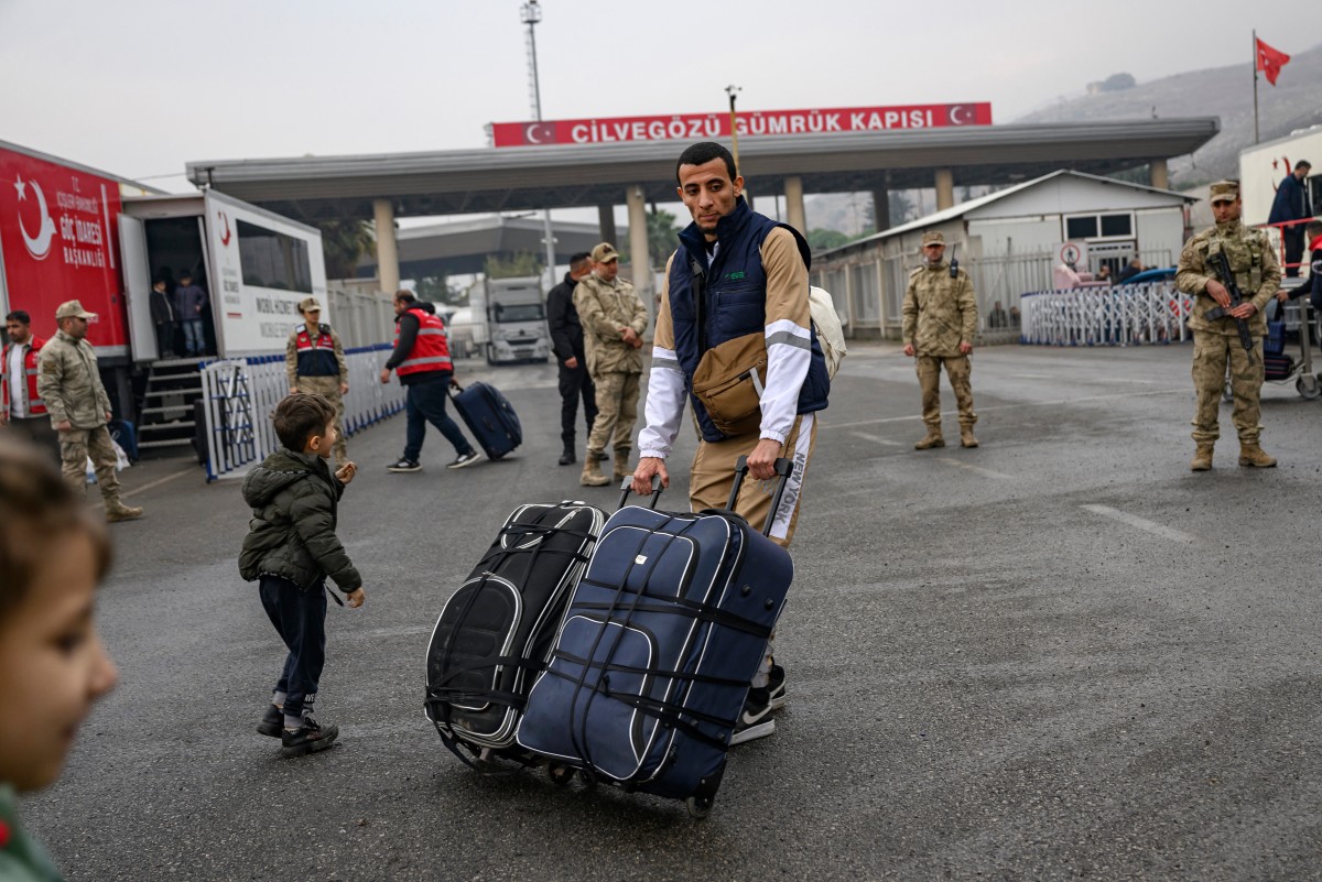 A Syrian living in Turkey pushes his suitcases at the Cilvegozu border crossing gate in Reyhanli on December 12, 2024, on the way back to his country following the oust of Syrian president. (AFP)