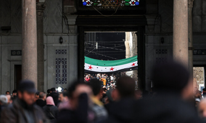 People walk as a flag adopted by the new Syrian rulers is seen, in the Umayyad Mosque, after Syria’s Bashar Assad was ousted, in Damascus, Syria, on December 27, 2024. (Reuters)
