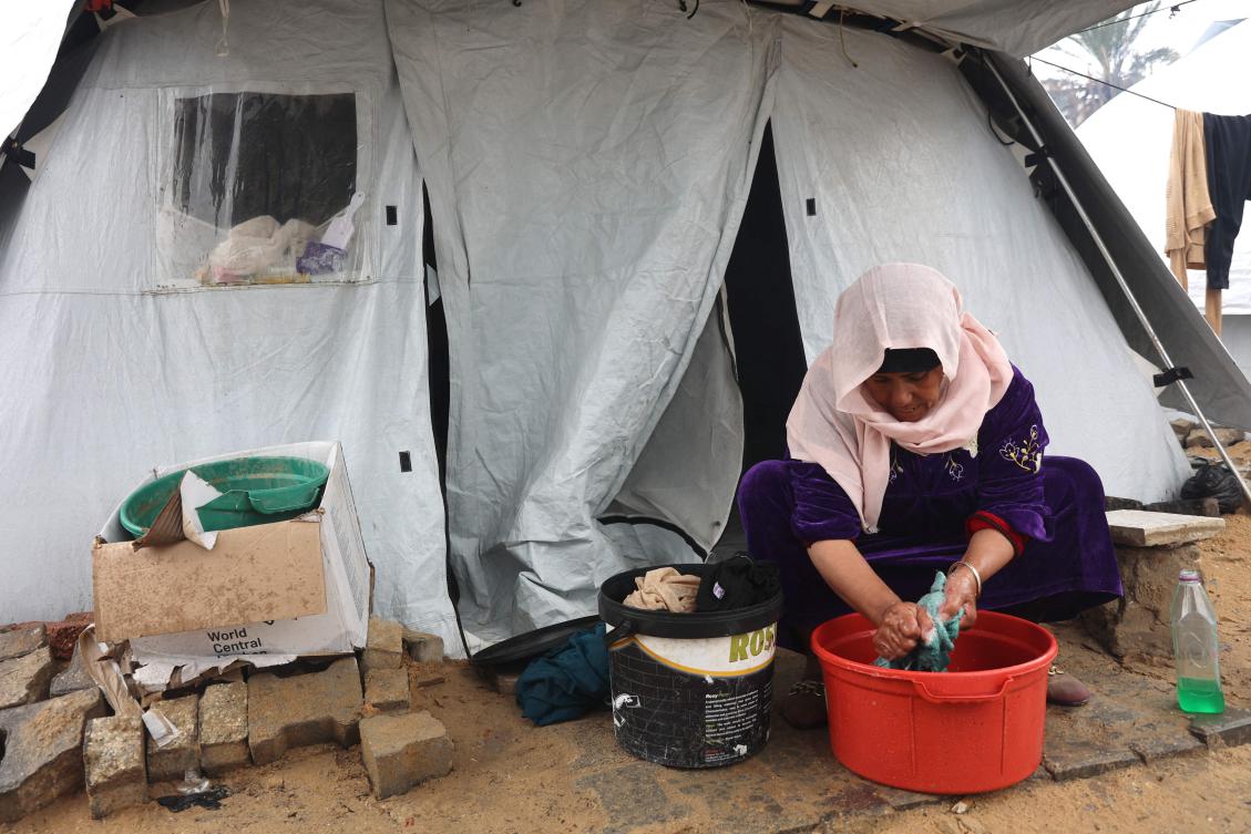 A Palestinian woman washes her clothes outside her tent at a makeshift camp for displaced Palestinians, during a storm in Gaza City on Dec. 31. (AFP)