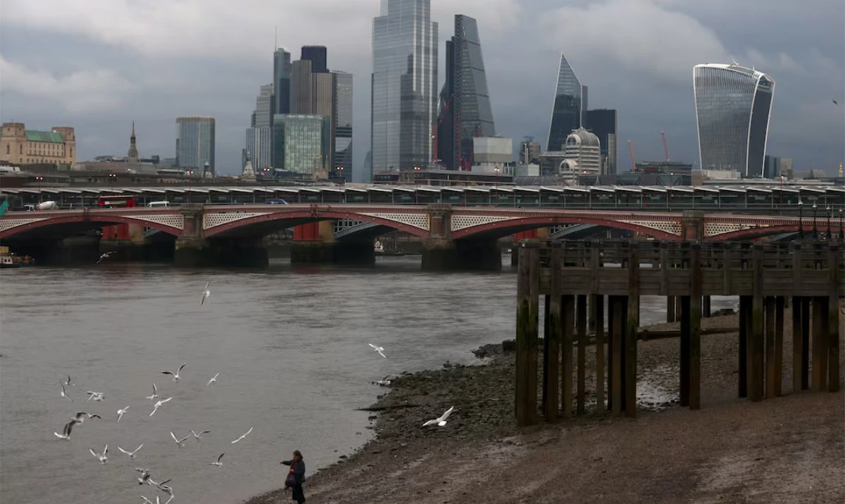A woman feeds birds on the bank of the river Thames with London's financial district seen in the background, amid the coronavirus disease (COVID-19) in London, Britain, November 25, 2020. (Reuters)