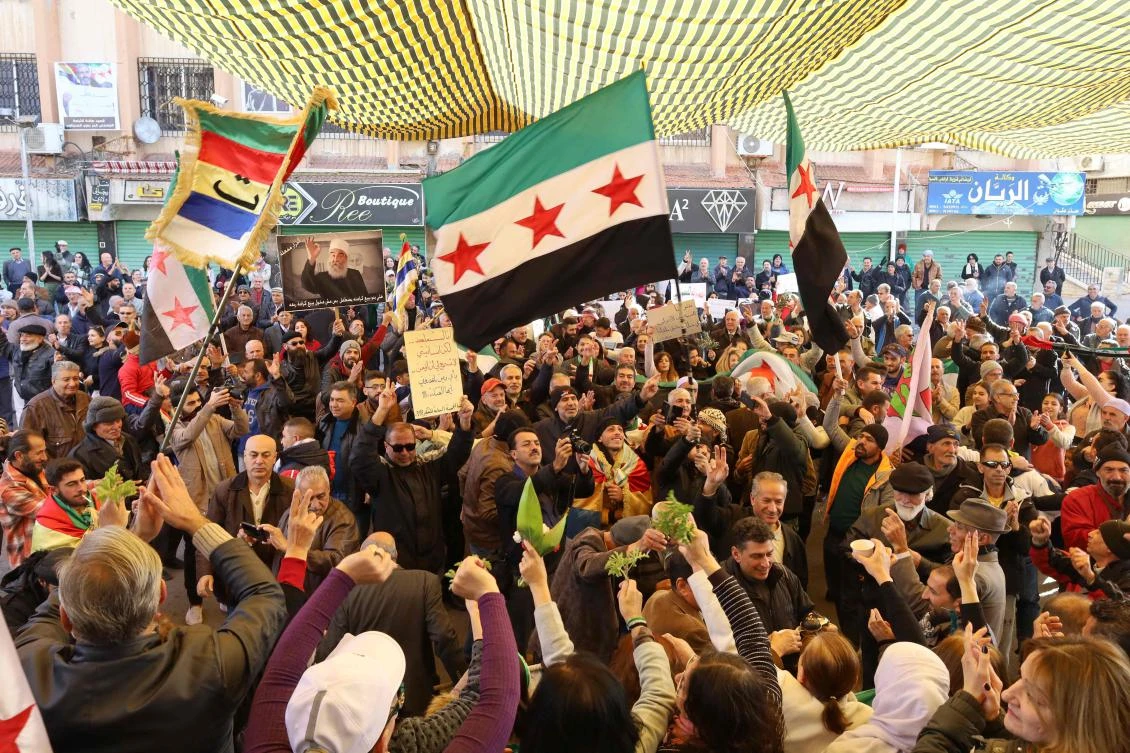 People chant slogans and wave the opposition flag during a gathering against the Syrian government in the Syria’s southern city of Sweida on Dec. 6, 2024. (AFP)