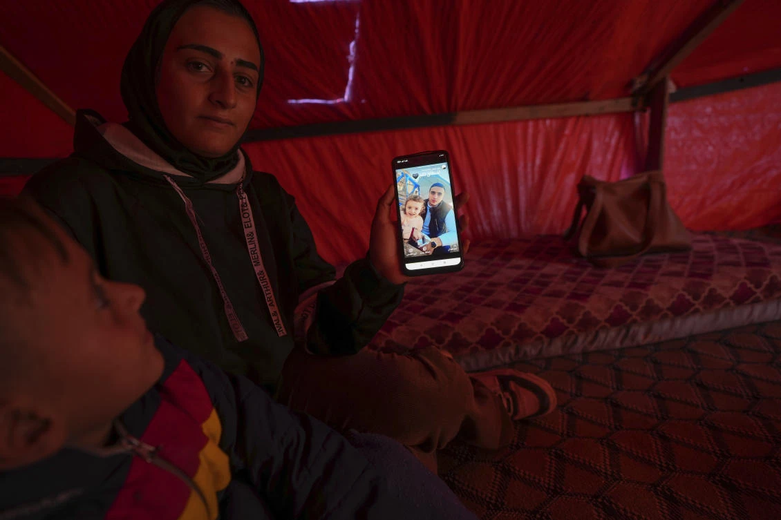 Sitting next to her son Wael, left, Reem Ajour shows a picture of her daughter, Masaa, and her husband, Talal, on her cellphone in a camp outside Zuweida, Gaza Strip, Nov. 20, 2024. (AP)