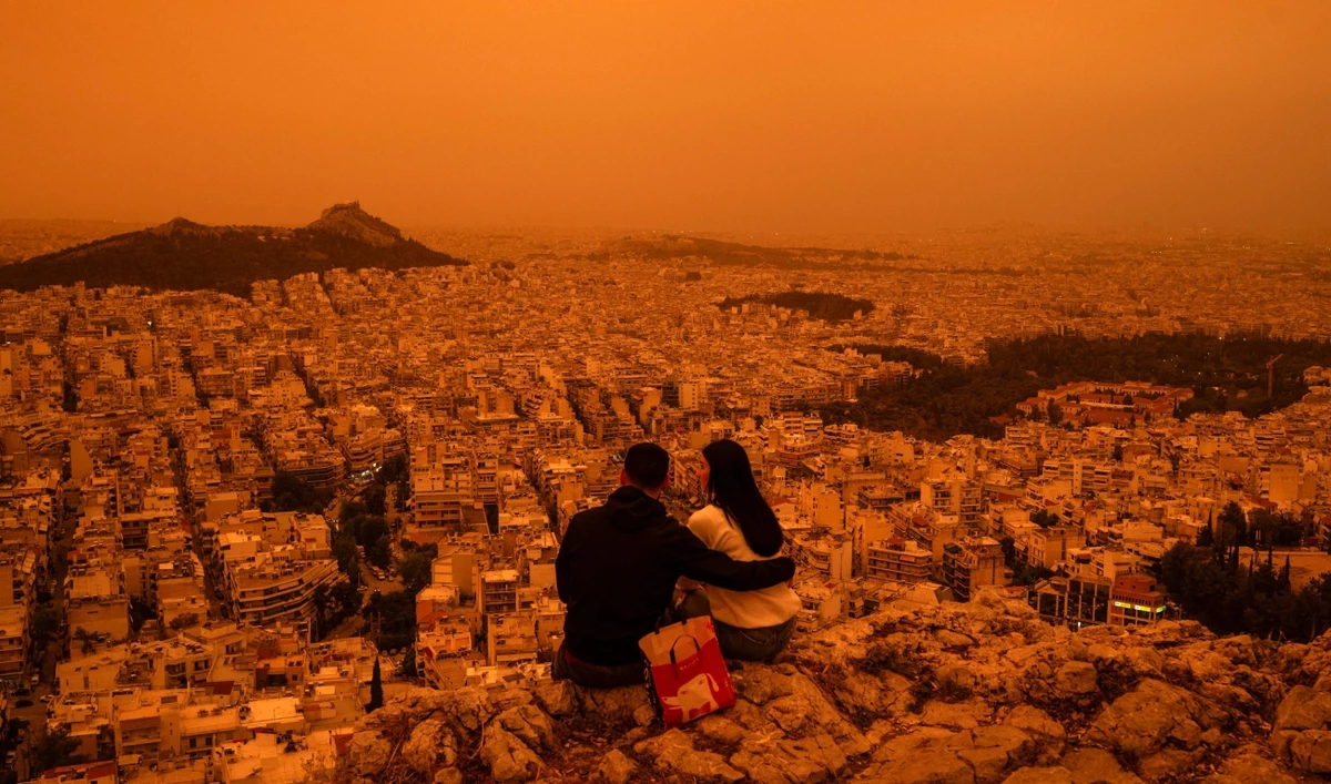 A couple sits on Tourkovounia hill, as southerly winds carry waves of Saharan dust, in Athens, on April 23, 2024. (AFP)