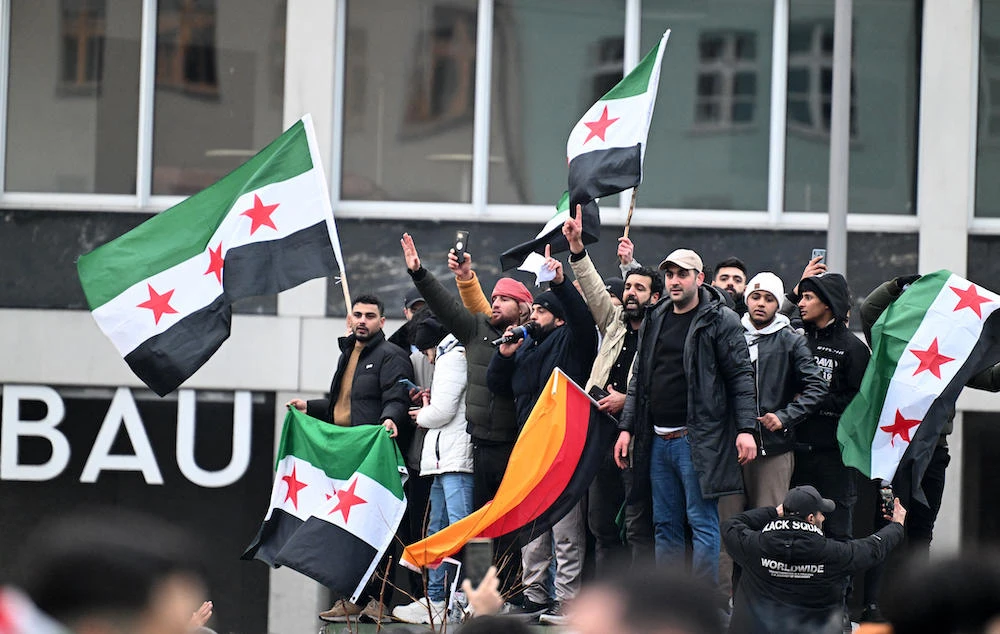 Members of the Syrian community hold flags of Syria and Germany as they rally on Dec. 8, 2024 in Berlin, Germany, to celebrate the end of Bashar Assad’s rule. (AFP)
