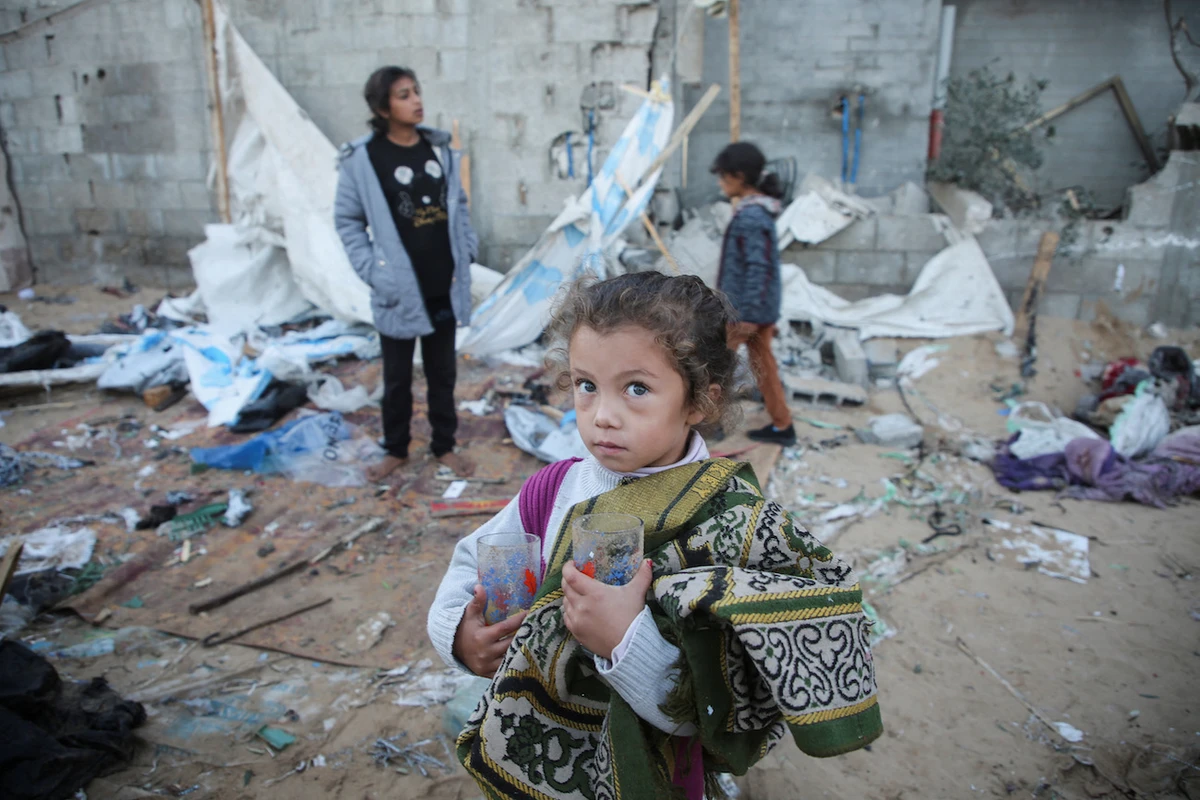 Palestinian girl holds glasses as she stands amid the damage at a tent camp sheltering displaced people, following an Israeli strike in Khan Younis, southern Gaza Strip, December 18, 2024. (Reuters)