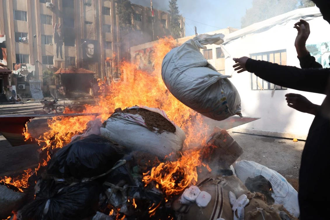 A man throws a bag onto a pile of burning illicit drugs, as Syria's new authorities burn drugs reportedly seized from a security branch, in Damascus on December 25, 2024. (AFP)