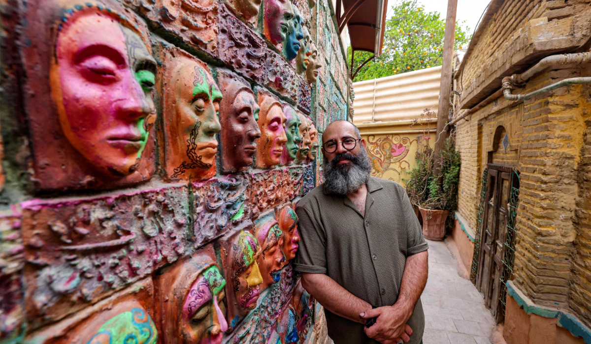 Adel Yazdi, an Iranian artist who has transformed an alley in one of the old neighbourhoods of Shiraz into an open air permanent art gallery, stands next to one of his high reliefs in the central Iranian city on May 14, 2024. (AFP)