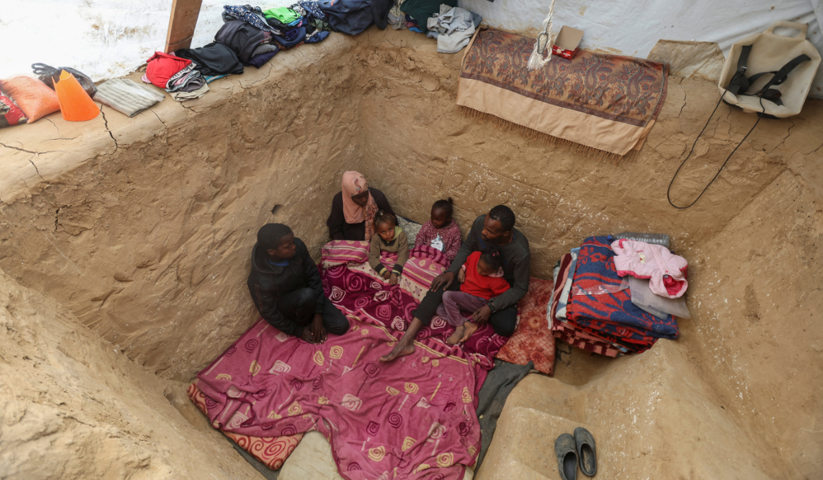 Displaced Palestinian man Tayseer Obaid sits with his family in an underground pit he dug at their tent encampment to protect them from Israeli strikes, in Deir Al-Balah, central Gaza Strip, January 6, 2025. (REUTERS)