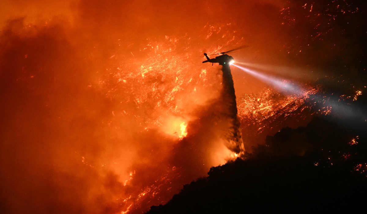 A fire fighting helicopter drops water as the Palisades fire grows near the Mandeville Canyon neighborhood and Encino, California, on January 11, 2025. (AFP)