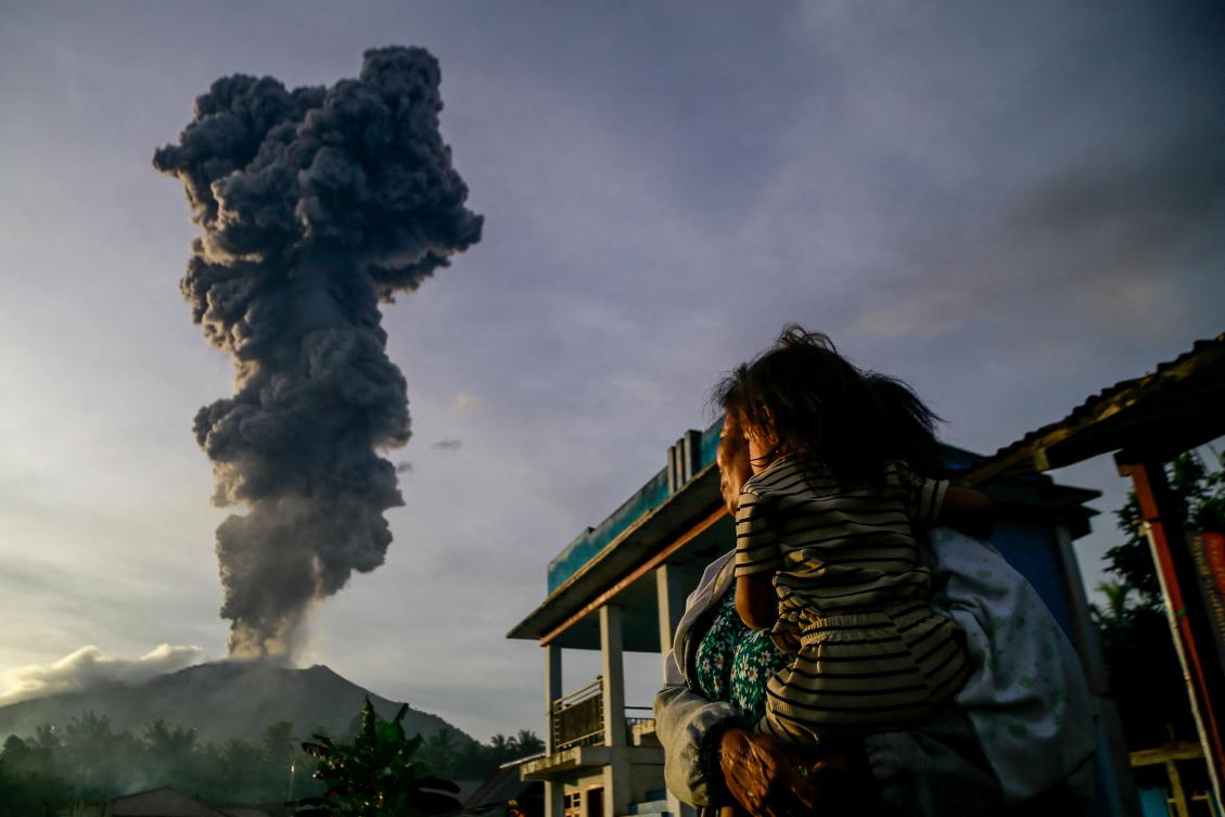 A woman and child look on at volcanic ash rising into the air during the eruption of Mount Ibu, as seen from Duono Village in West Halmahera, North Maluku province, on January 15, 2025. (AFP)