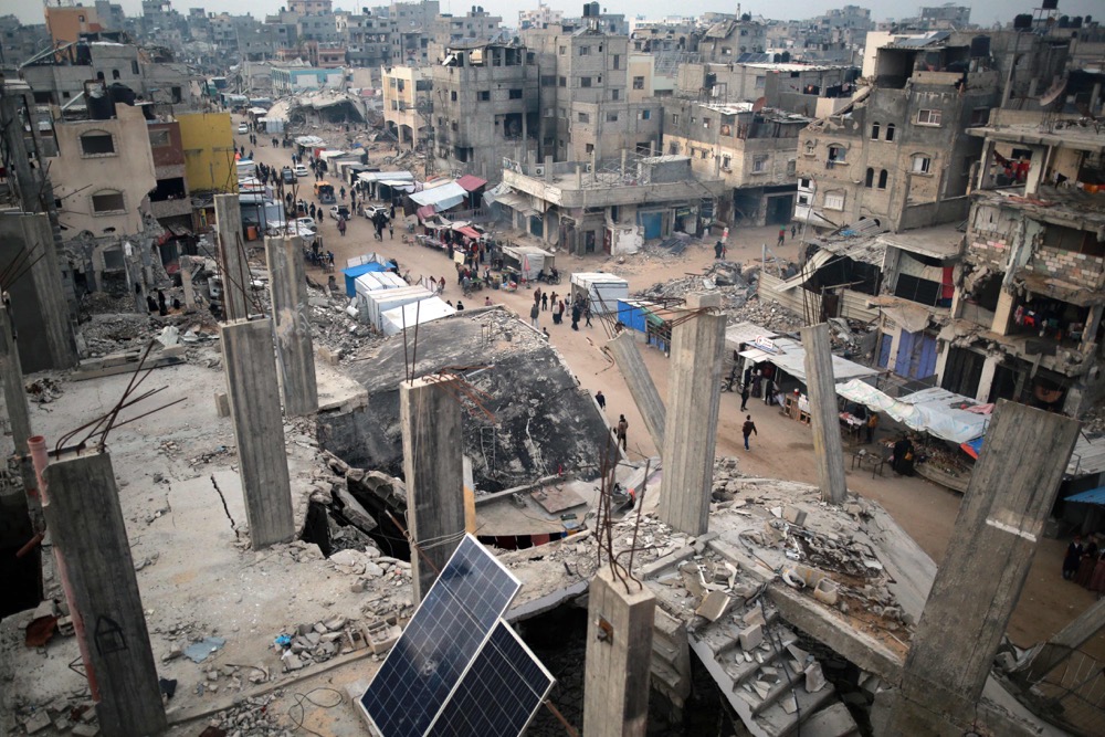 People walk past stalls selling goods amid the rubble of buildings destroyed during previous Israeli strikes, in Khan Yunis in the southern Gaza Strip. (AFP)