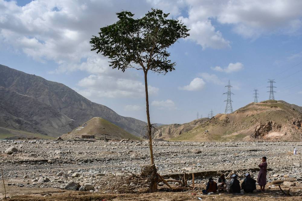 People sit near a tree, following flash floods after heavy rainfall in Dahane Larkhab area in Dushi district of Baghlan province on May 26, 2024. (AFP)