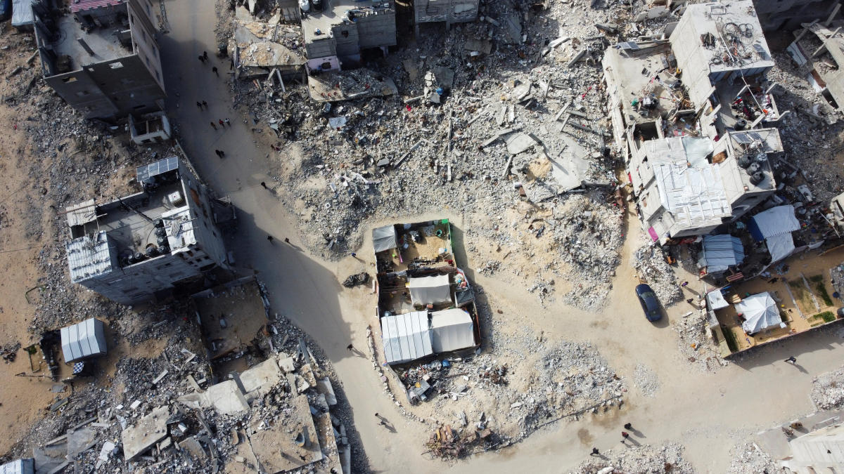 A drone view shows Palestinians walking past the rubble of houses and buildings destroyed in Israeli strikes during the war, in Khan Younis in the southern Gaza Strip, January 20, 2025. (Reuters)