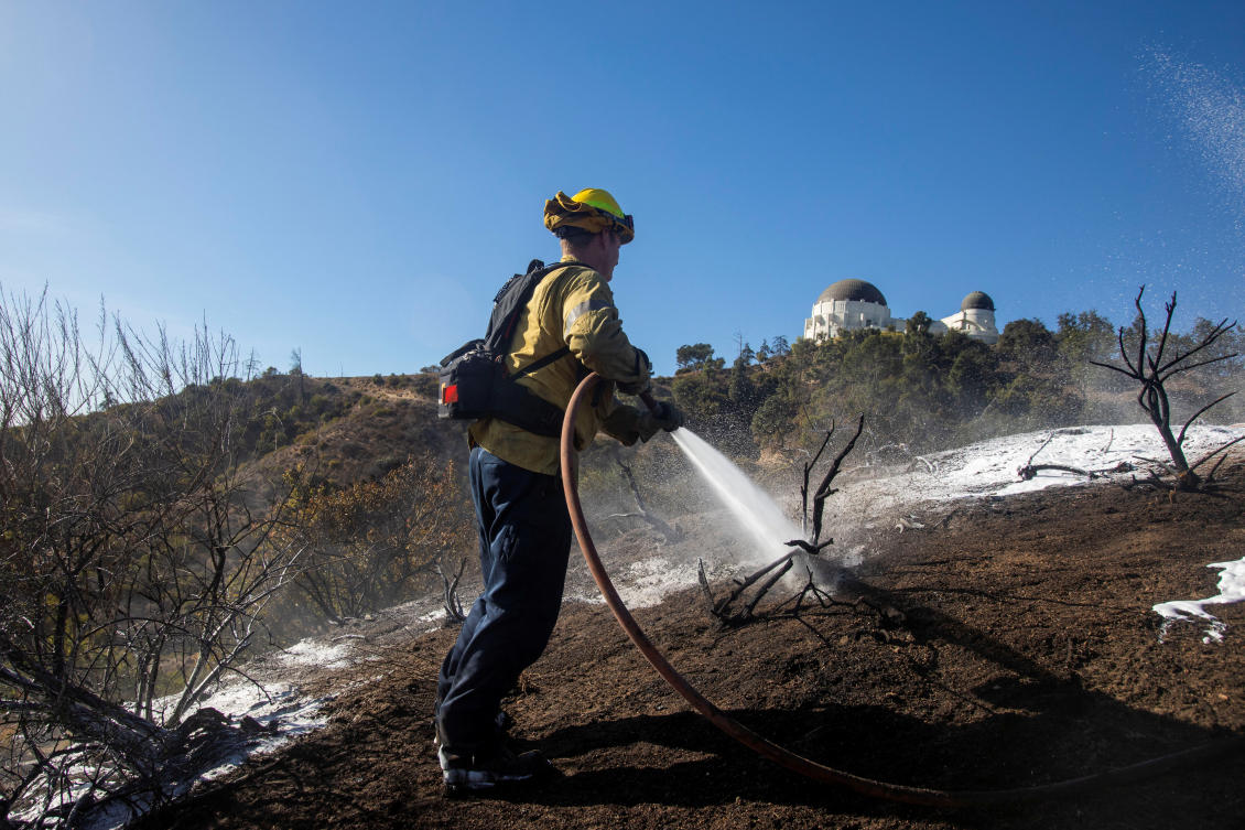 A firefighter works on hot spots after a brush fire burned in Griffith Park on a slope below the Griffith Observatory, Los Angeles, California. (Reuters)