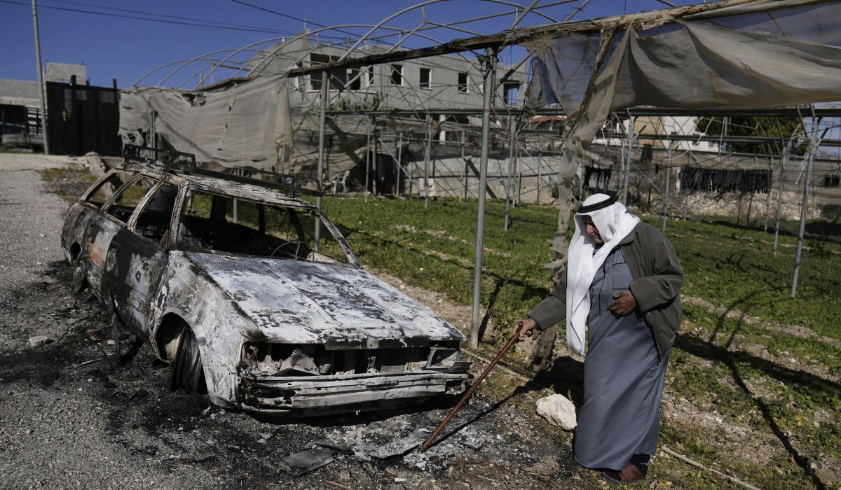 A Palestinian stands beside a torched car in the aftermath of an attack by Israeli settlers in the West Bank village of Jinsafut, Tuesday, Jan. 21, 2025. (AP)