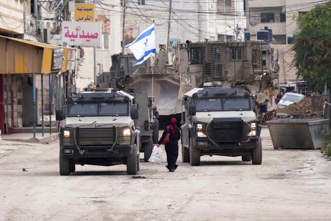 A Palestinian woman walks past Israeli army vehicles during a military raid in Jenin in the occupied West Bank, on January 22, 2025.(AFP)