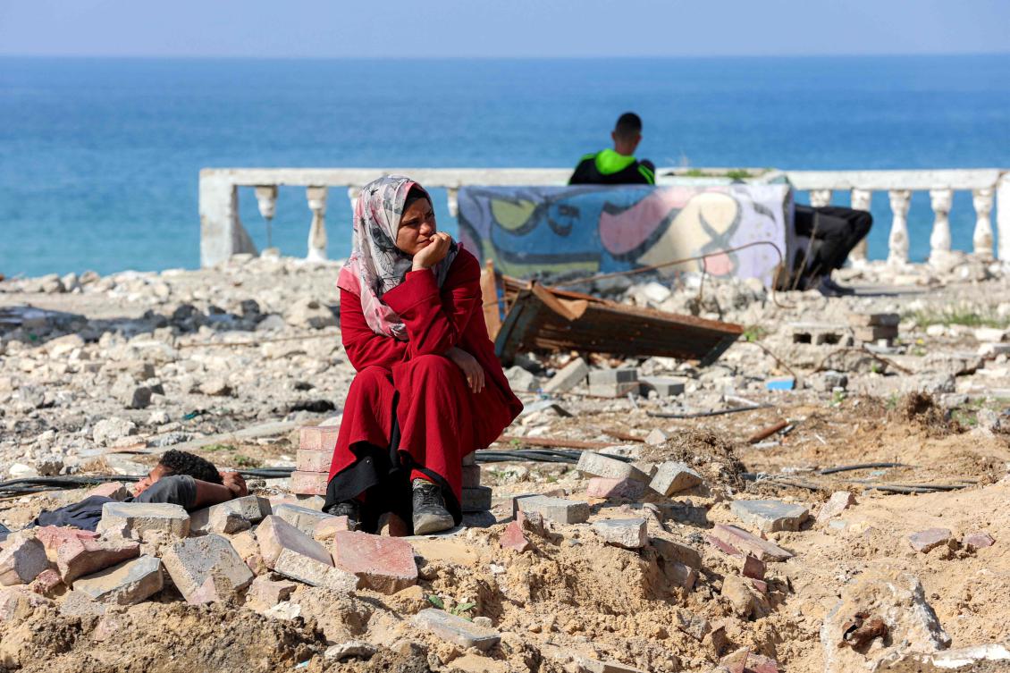 A woman sits by rubble as she waits along Gaza's coastal al-Rashid Street for people to cross from the Israeli-blocked Netzarim corridor from the southern Gaza Strip into Gaza City, Jan. 26 (AFP)