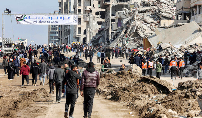 People gather by a banner welcoming people near the rubble of a collapsed building along Gaza's coastal al-Rashid Street for people to cross from the Israeli-blocked Netzarim corridor from the southern Gaza Strip into Gaza City on January 26, 2025. (AFP)