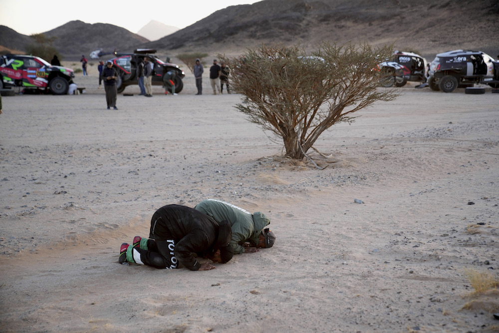 Toyota driver Yazeed Al Rajhi, left, and Ford driver Nasser Al-Attiyah pray at the bivouac after the stage two, day one of the Dakar Rally in Bisha, Saudi Arabia on Jan. 5, 2025. (AP)