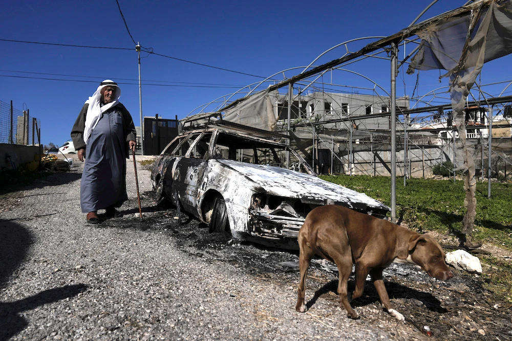 A Palestinian stands beside a car torched by Israeli settlers in the West Bank village of Jinsafut on Jan. 21, 2025. (AP)