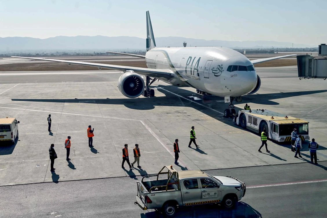 Ground staff stand next to the Pakistan International Airline aircraft ahead of its takeoff for Paris at the Islamabad International Airport on Jan. 10, 2025. (AFP)