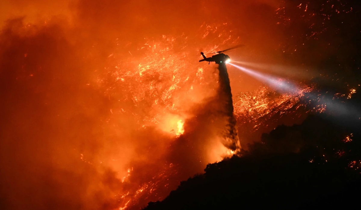 A fire fighting helicopter drops water as the Palisades fire grows near the Mandeville Canyon neighborhood and Encino, California, on January 11, 2025. (AFP)