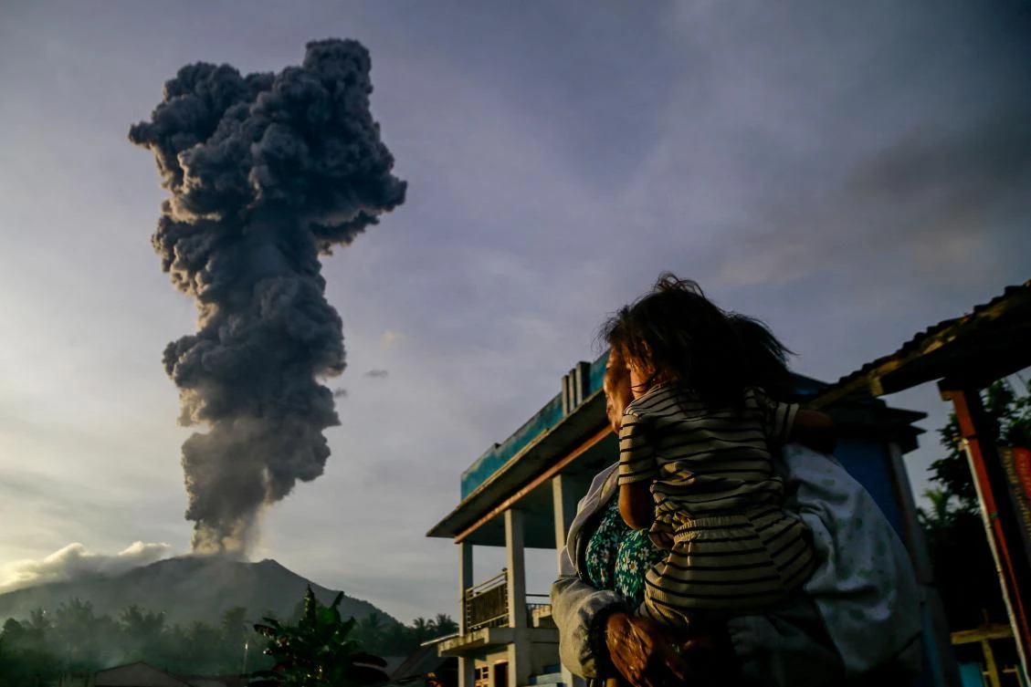 A woman and child look on at volcanic ash rising into the air during the eruption of Mount Ibu, as seen from Duono Village in West Halmahera, North Maluku province, on January 15, 2025. (AFP)
