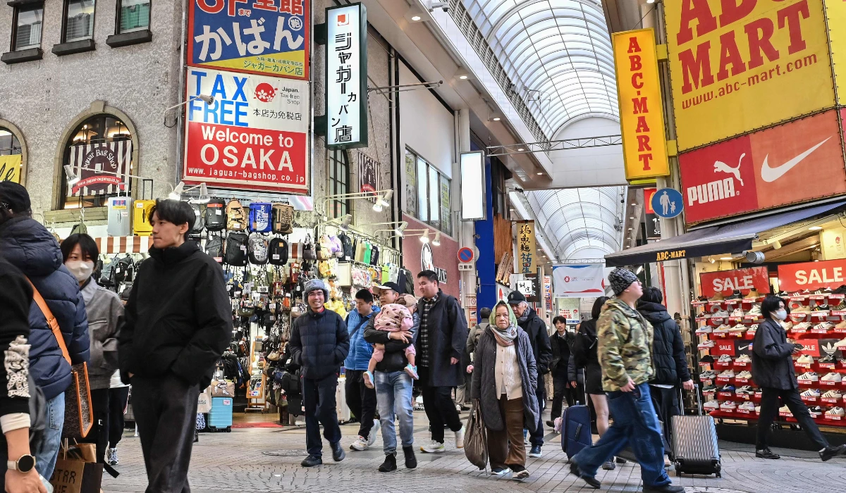People walk past a large sign (top L) advertising tax-free shopping for tourists, in a commercial area in central Osaka on January 19, 2025. (AFP)