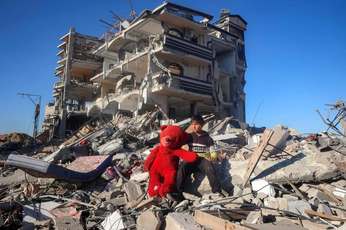 A boy sits with a rescued giant red teddy bear doll on rubble near a heavily-damaged building in Rafah in the southern Gaza Strip on Jan. 21, 2025, as residents return following a ceasefire deal. (AFP)
