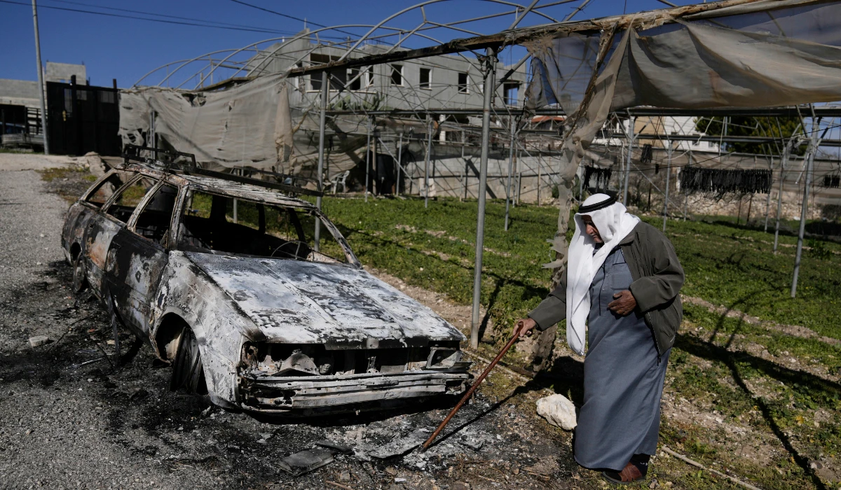 A Palestinian stands beside a torched car in the aftermath of an attack by Israeli settlers in the West Bank village of Jinsafut, Tuesday, Jan. 21, 2025. (AP)
