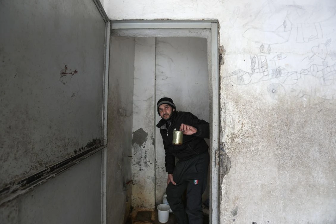 Former detainee in Sednaya Mohammed Najib sits across from a discarded portrait of ousted Syrian president Bashar al-Assad, in front of a facility which was used as a jail for the Tishreen Military Hospital, currently out of service, in Damascus on January 10, 2025. (AFP)
