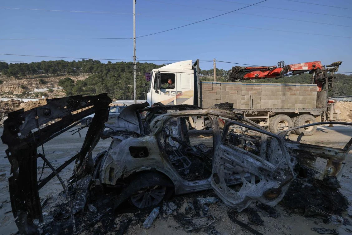 Palestinians drive their vehicles past the carcass of a car that was destroyed in an Israeli airstrike in the Nur Shams refugee camp near Tulkarem in the occupied West Bank on January 27, 2025. (AFP)