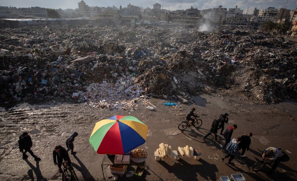Palestinians walk past a pile of smoldering garbage in Gaza City, Wednesday, Feb. 12, 2025. (AP Photo)