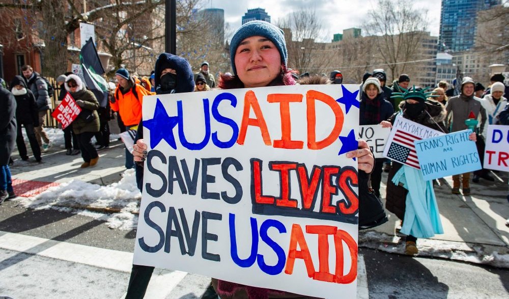 A woman holds a sign supporting USAID at an anti-Donald Trump policy rally on Presidents’ Day, Boston, Feb. 17, 2025. (AFP)