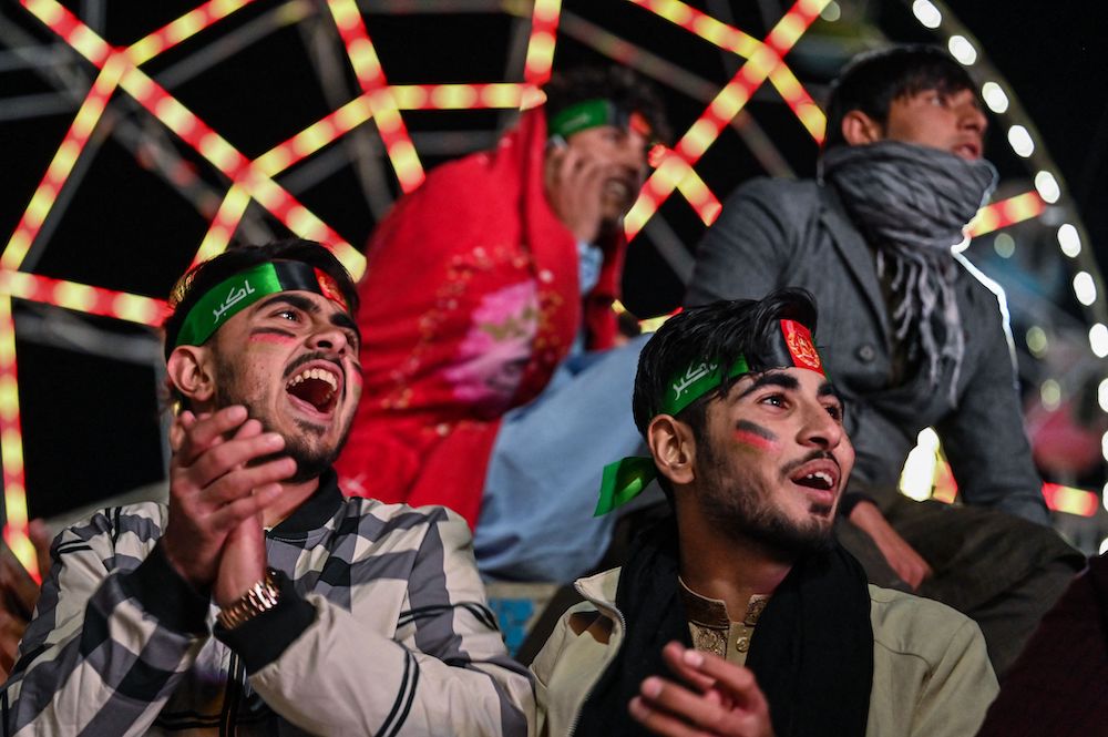 Spectators, wearing headbands with the Afghan national flag, react as they watch on Afghanistan playing a cricket match against Pakistan on screen, in the outskirts of Kabul on Oct. 29, 2021. (AFP)