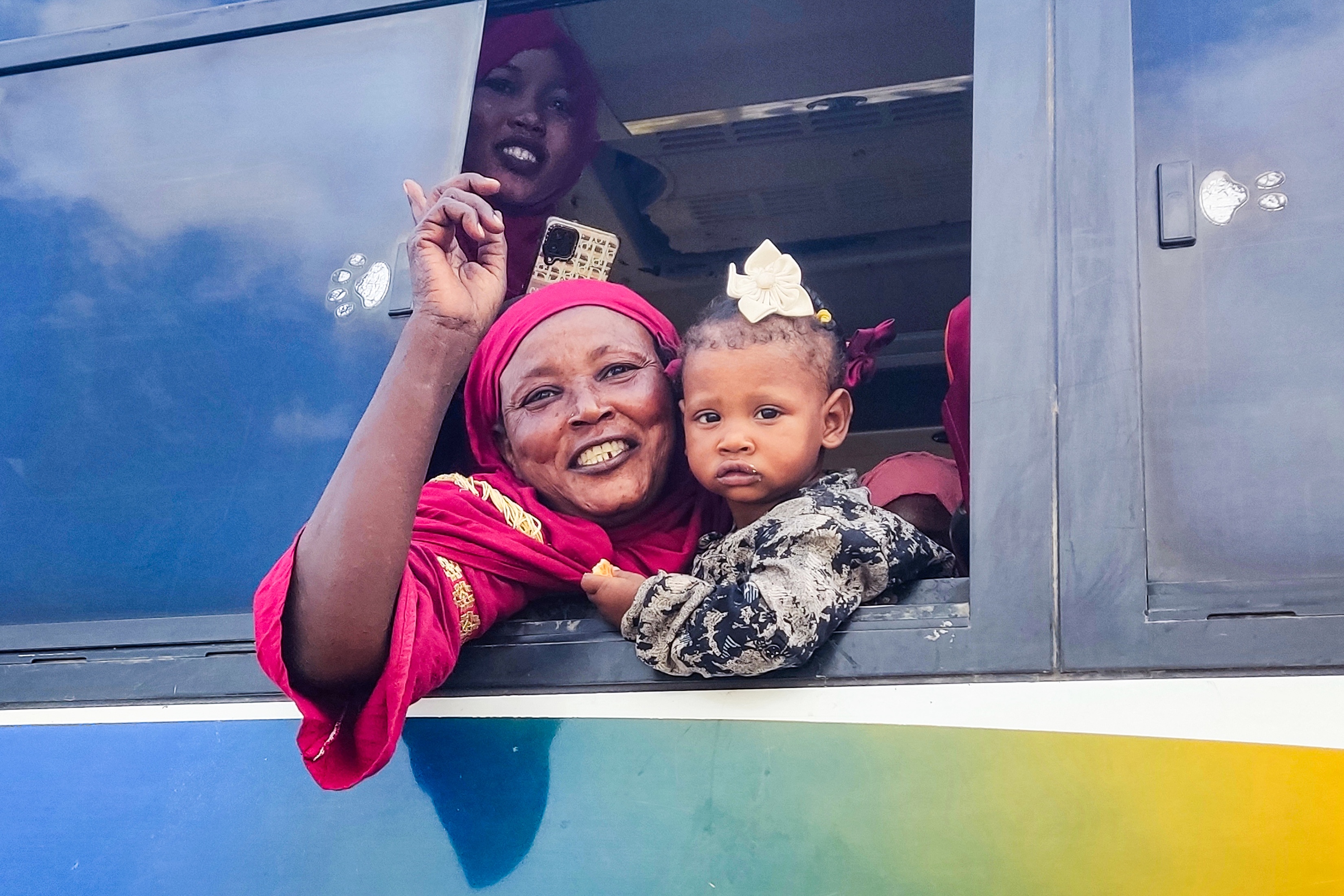 People displaced by conflict bid farewell to locals from Port Sudan in northeastern Sudan as they embark to return home by bus to the southern city of Singah in Sennar province, December 2024 (AFP)