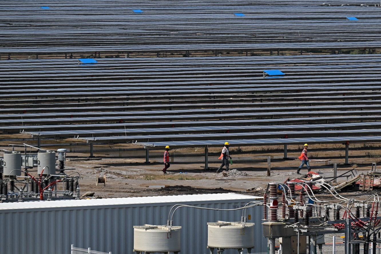 Workers walk past solar panels installed at the Adani Green Renewable Energy Plant in Khavda, in India's Gujarat state on Oct. 15, 2024. (AFP)