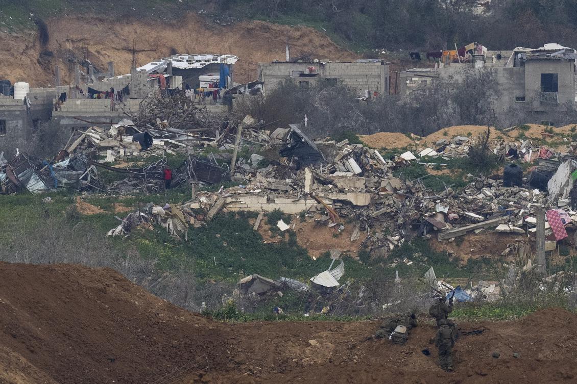 A Palestinian man wearing a red shirt, left, stands amidst the rubble of destroyed buildings, watching Israeli soldiers, bottom right, take position in the northern Gaza Strip, as seen from southern Israel. (AP)